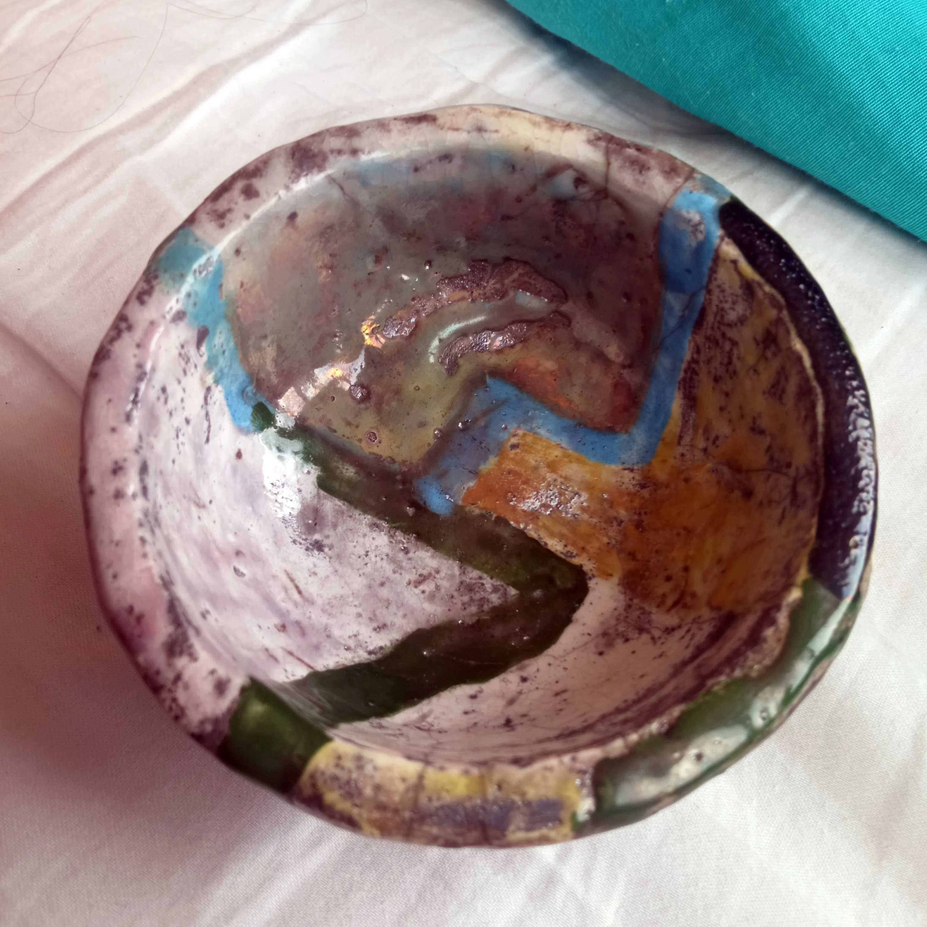 Shallow raku bowl painted with pink, blue, green and ochre geometric zigzag bands, viewed from above.