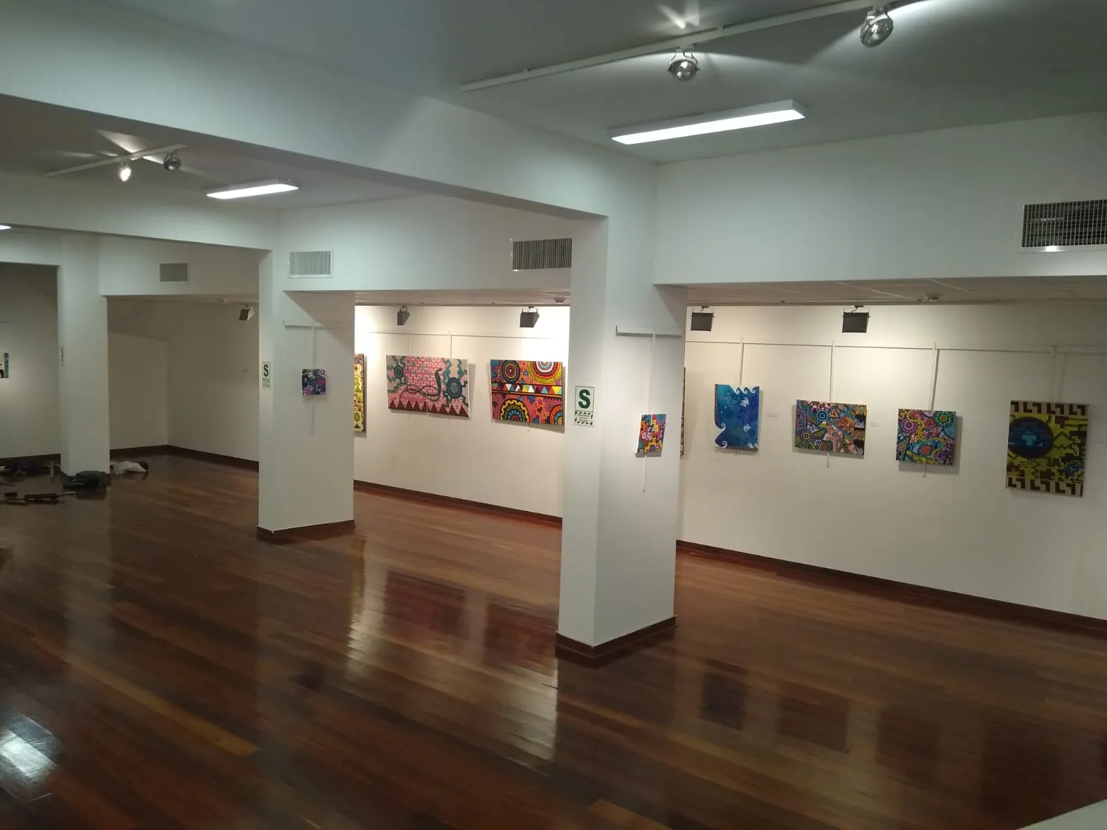 Wide view of the Unife Art Gallery in Lima with rows of Ximena Heraud's colorful geometric works hung along the walls